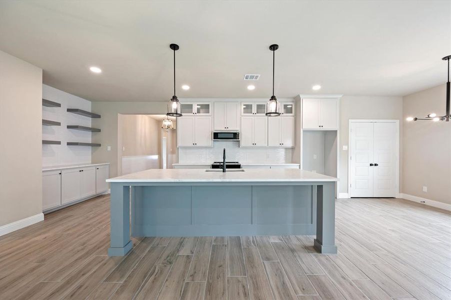 Kitchen with decorative light fixtures, white cabinetry, decorative backsplash, light wood-type tile flooring, and a kitchen island with sink