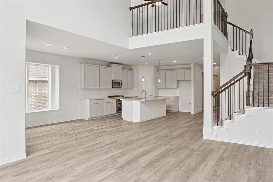 Unfurnished living room with a high ceiling, sink, light wood-type flooring, and ceiling fan