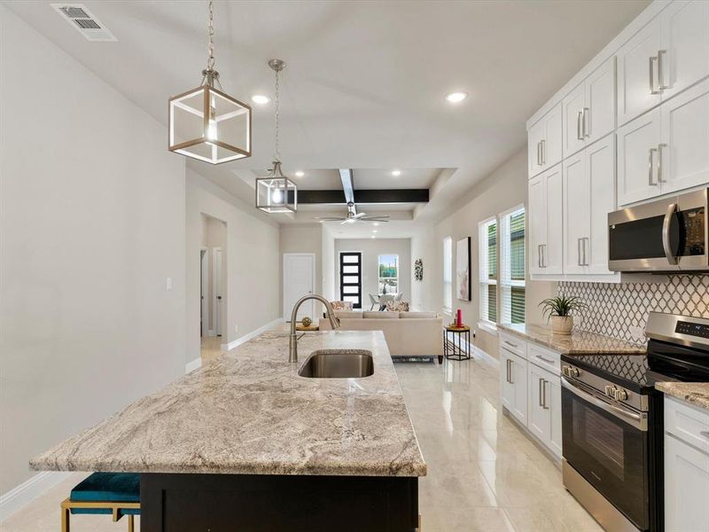 Kitchen with ceiling fan, a large island, decorative light fixtures, white cabinetry, and appliances with stainless steel finishes