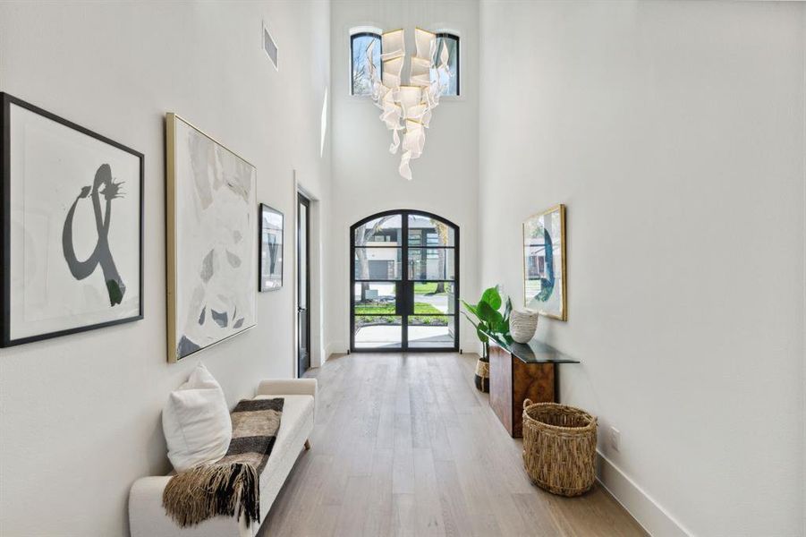 Entrance foyer with french doors, a towering ceiling, a chandelier, and light hardwood / wood-style floors