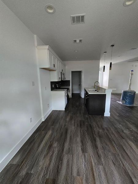 Kitchen featuring pendant lighting, an island with sink, a textured ceiling, dark wood-type flooring, and white cabinetry