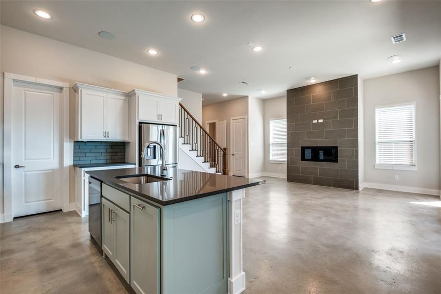 Kitchen featuring tasteful backsplash, sink, a tile fireplace, white cabinetry, and a center island with sink