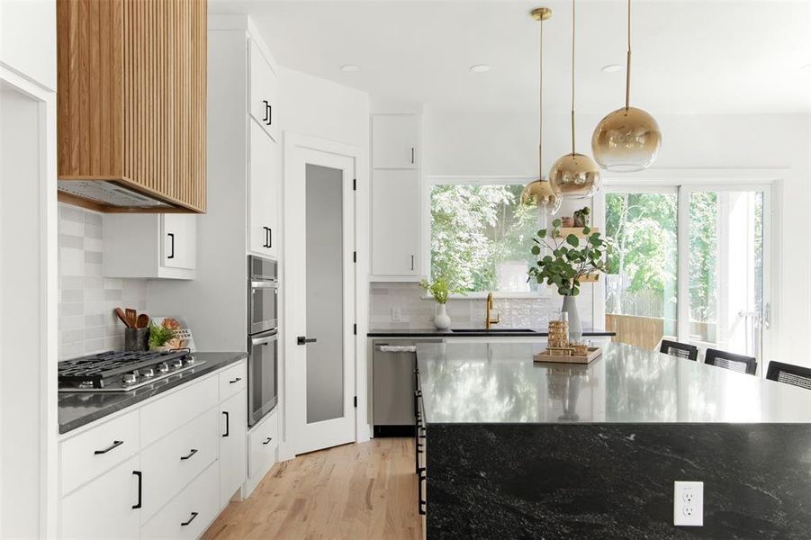 Kitchen with backsplash, white cabinetry, light hardwood / wood-style flooring, and decorative light fixtures