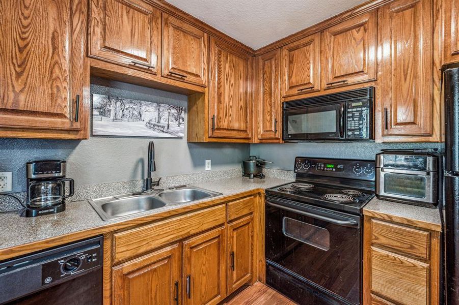 Kitchen featuring sink, black appliances, a textured ceiling, and light hardwood / wood-style floors