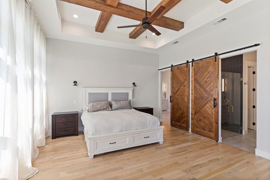 Bedroom with ceiling fan, ensuite bath, light wood-type flooring, a barn door, and coffered ceiling