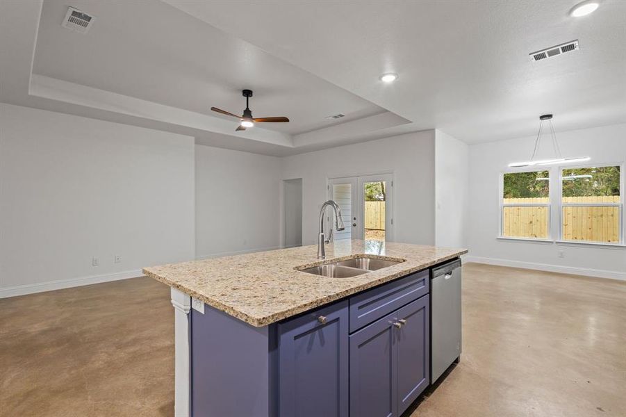 Kitchen featuring sink, a tray ceiling, decorative light fixtures, stainless steel dishwasher, and a center island with sink