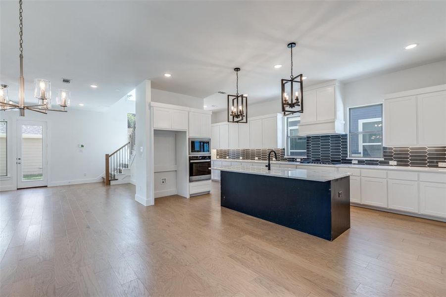 Kitchen with white cabinetry, a kitchen island with sink, pendant lighting, and stainless steel oven