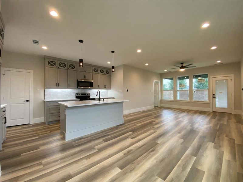 Kitchen with stainless steel appliances, hardwood / wood-style flooring, ceiling fan, and a kitchen island with sink