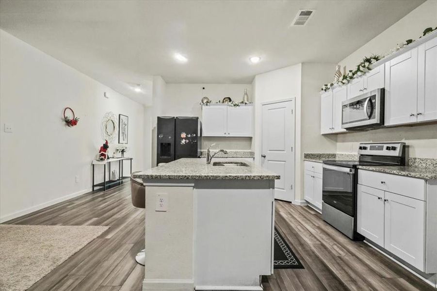 Kitchen with appliances with stainless steel finishes, a kitchen island with sink, sink, white cabinets, and dark hardwood / wood-style floors