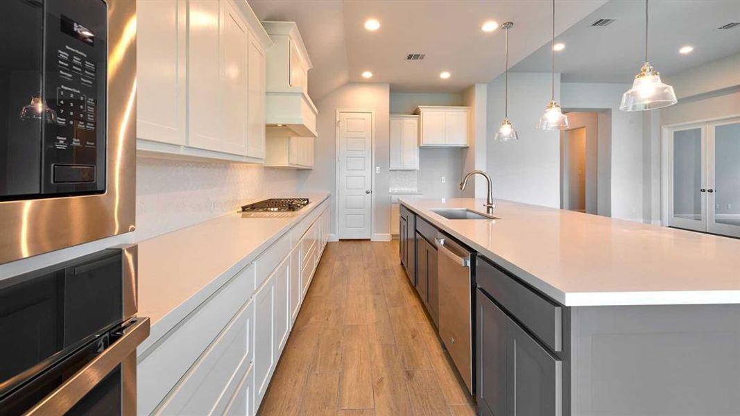 Kitchen featuring light hardwood / wood-style floors, tasteful backsplash, and a kitchen island with sink