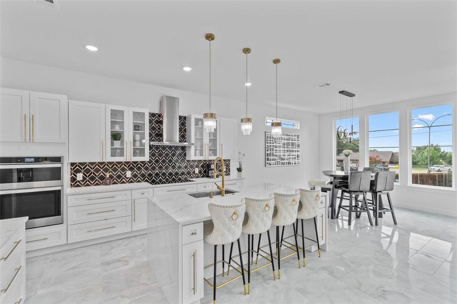 Kitchen featuring sink, a kitchen island with sink, wall chimney range hood, white cabinetry, and stainless steel double oven