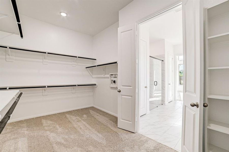 View of the primary closet with custom built-in wall safe, shelving and double doors.