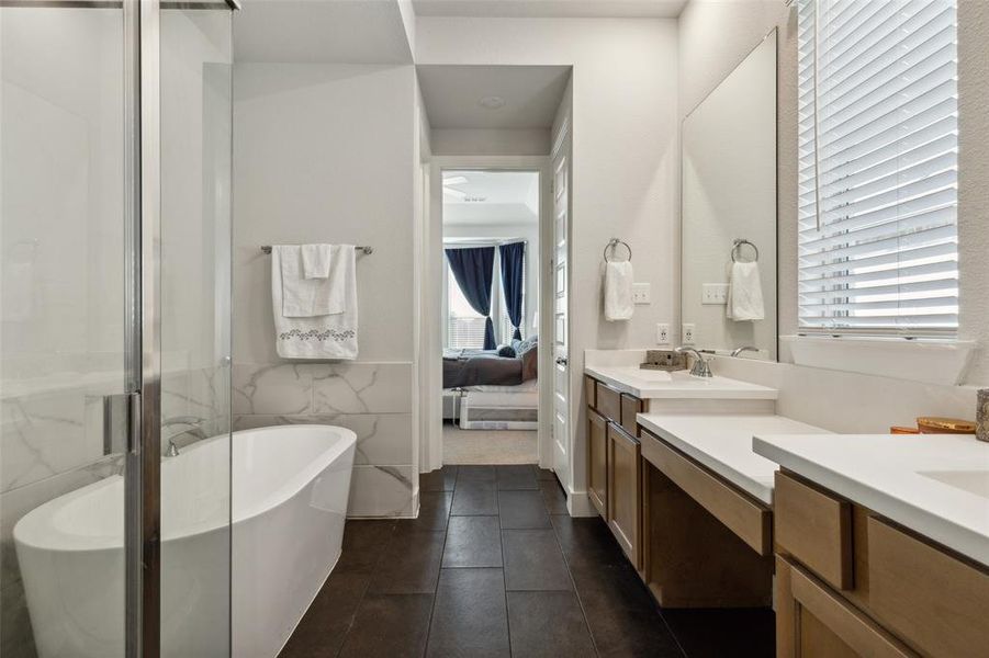 Primary bathroom with tile patterned flooring, tile walls, double vanity, and independent shower and  free-standing bath tub.