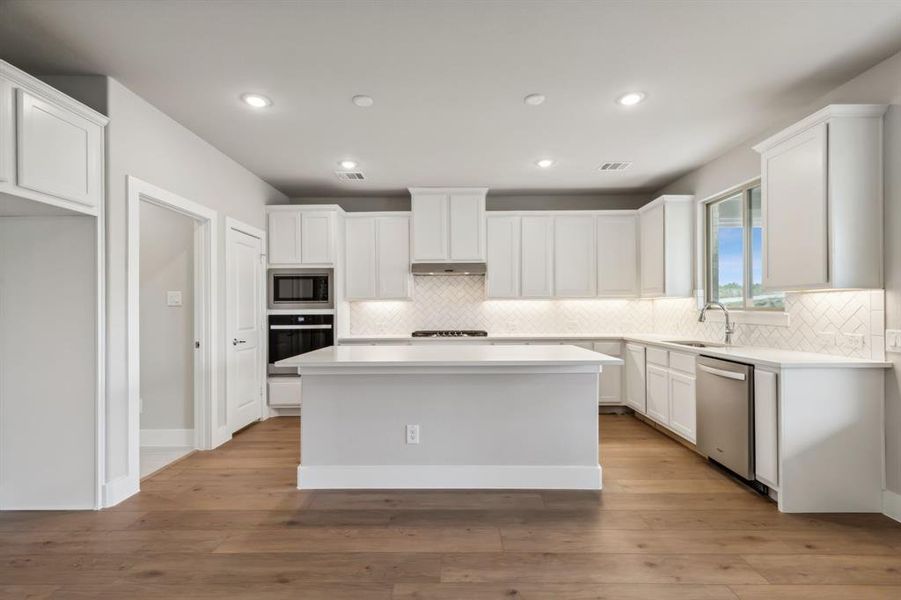 Kitchen with white cabinetry, stainless steel appliances, light wood-type flooring, a center island, and sink