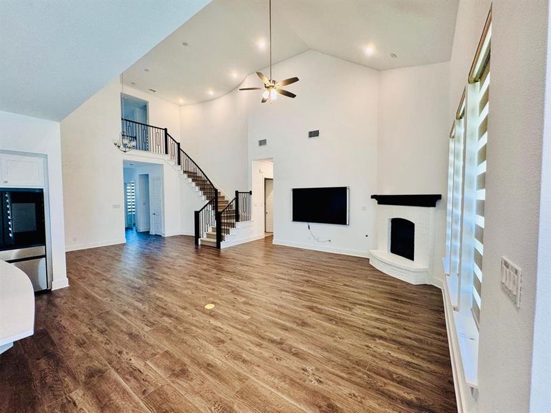 Unfurnished living room with ceiling fan, high vaulted ceiling, wood-type flooring, and a brick fireplace