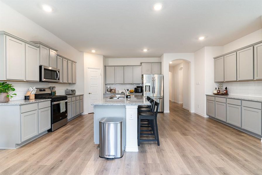 Kitchen with light hardwood / wood-style floors, light stone countertops, stainless steel appliances, and an island with sink