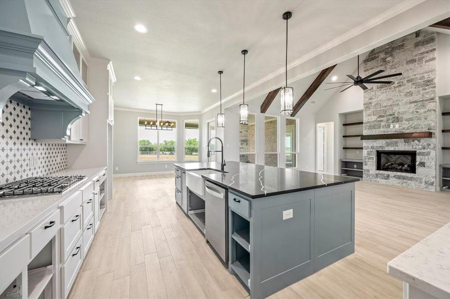 Kitchen featuring white cabinets, stainless steel appliances, a stone fireplace, a kitchen island with sink, and ceiling fan with notable chandelier