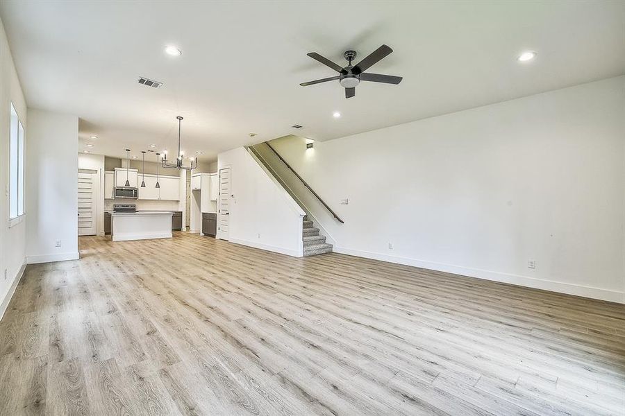 Unfurnished living room with ceiling fan with notable chandelier and light hardwood / wood-style flooring