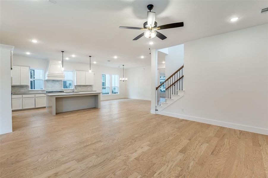 Unfurnished living room with light wood-type flooring, sink, and ceiling fan with notable chandelier