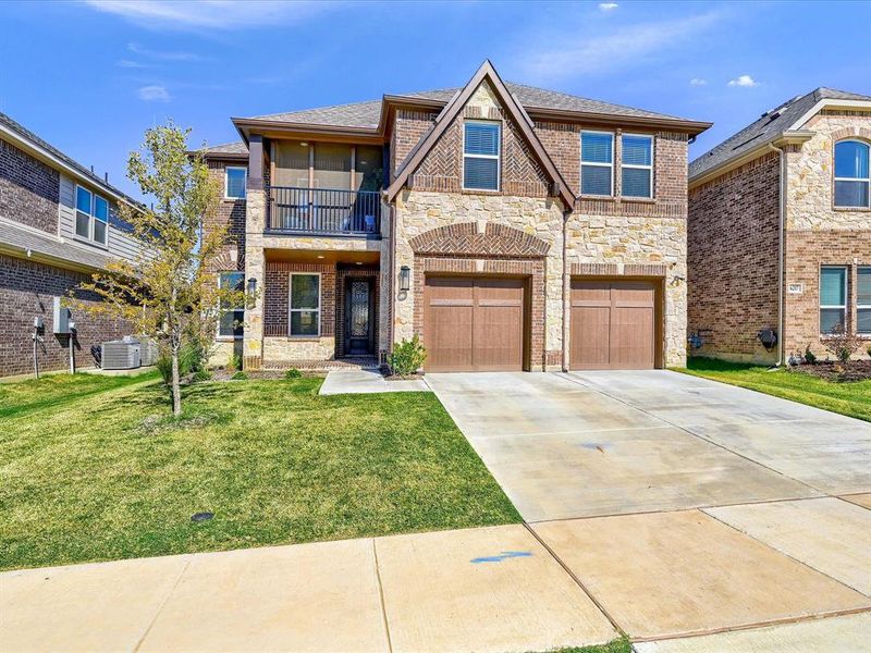 View of front of house featuring cooling unit, a balcony, a front lawn, and a garage