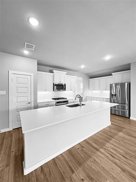 Kitchen with stainless steel appliances, sink, white cabinetry, hardwood / wood-style flooring, and a spacious island