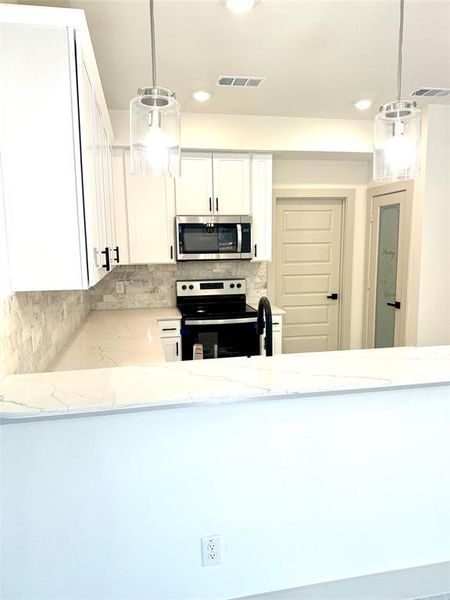 Kitchen with appliances with stainless steel finishes, white cabinets, light stone counters, and pendant lighting