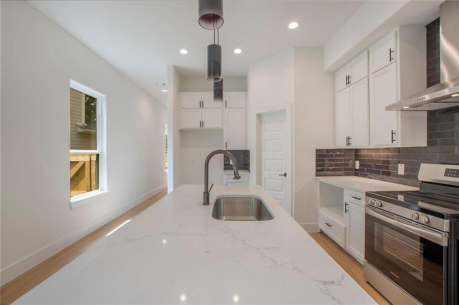 Kitchen featuring pendant lighting, sink, wall chimney range hood, white cabinetry, and stainless steel stove