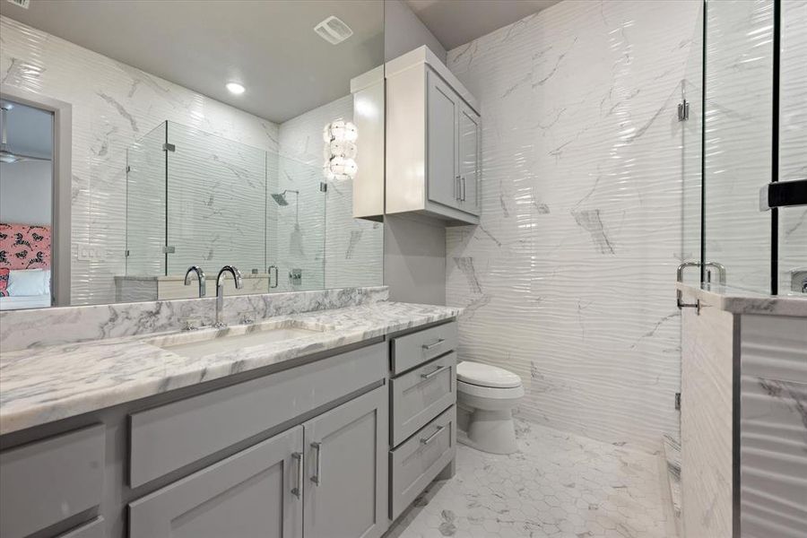 Bathroom with a shower with shower door, toilet, tile walls, and vanity