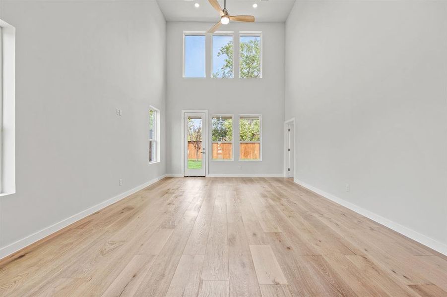 Unfurnished living room featuring ceiling fan, light wood-type flooring, and a towering ceiling