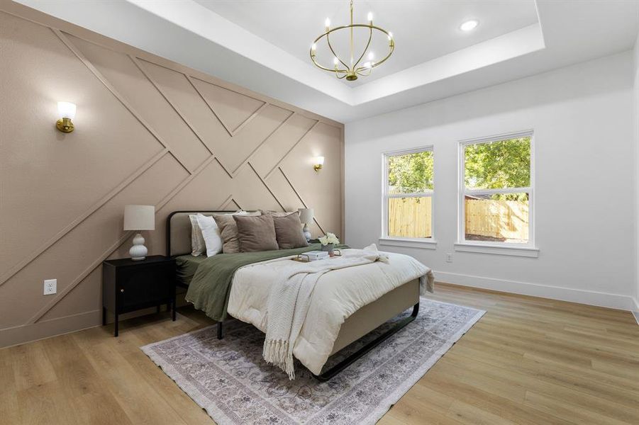 Bedroom with light hardwood / wood-style flooring, a notable chandelier, and a tray ceiling