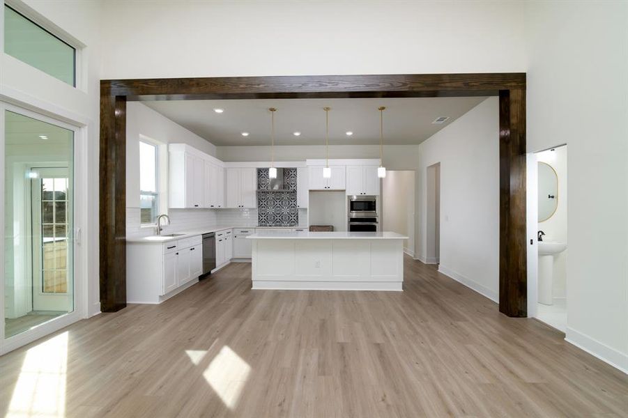 Kitchen with light hardwood / wood-style floors, a kitchen island, white cabinets, backsplash, and pendant lighting