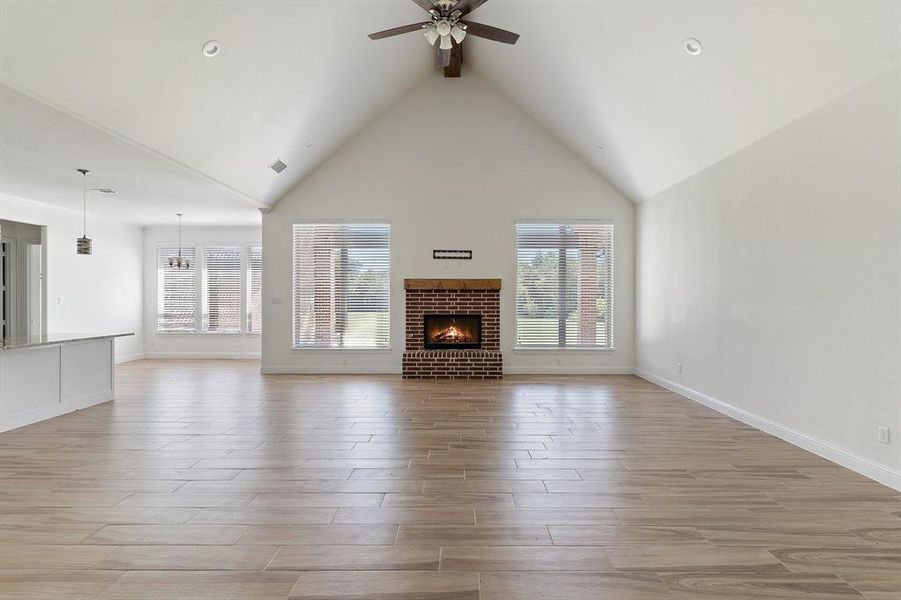 Unfurnished living room featuring light wood-type flooring, a brick fireplace, ceiling fan, and high vaulted ceiling