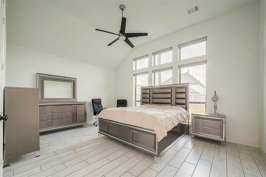 This is a spacious, well-lit bedroom featuring large windows, a high ceiling with a ceiling fan, and modern light-toned flooring.