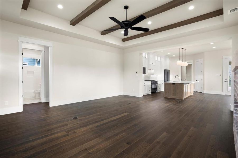 Unfurnished living room featuring dark wood-type flooring, ceiling fan, beamed ceiling, and sink