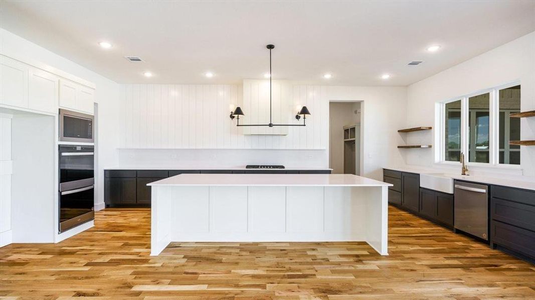 Kitchen featuring a kitchen island, sink, pendant lighting, appliances with stainless steel finishes, and light hardwood / wood-style floors