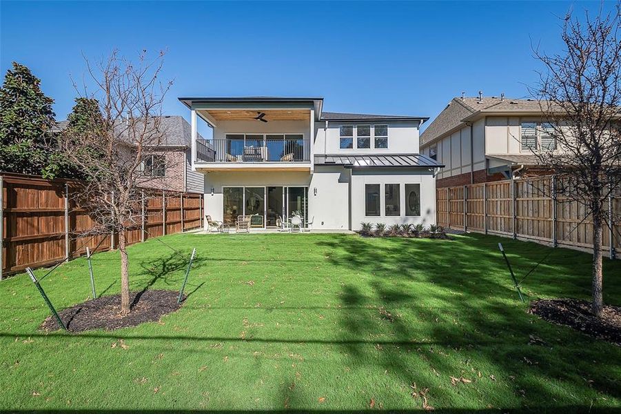 Rear view of house featuring a lawn, ceiling fan, and a balcony