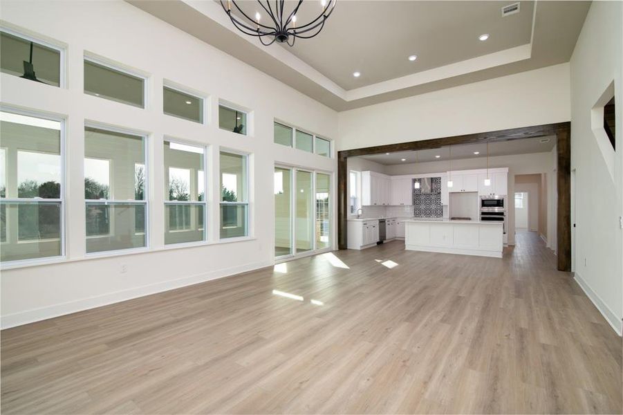 Unfurnished living room with a towering ceiling, light wood-type flooring, a chandelier, and a raised ceiling