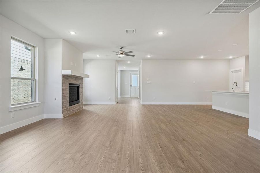 Unfurnished living room with light hardwood / wood-style flooring, a tiled fireplace, ceiling fan, and a healthy amount of sunlight