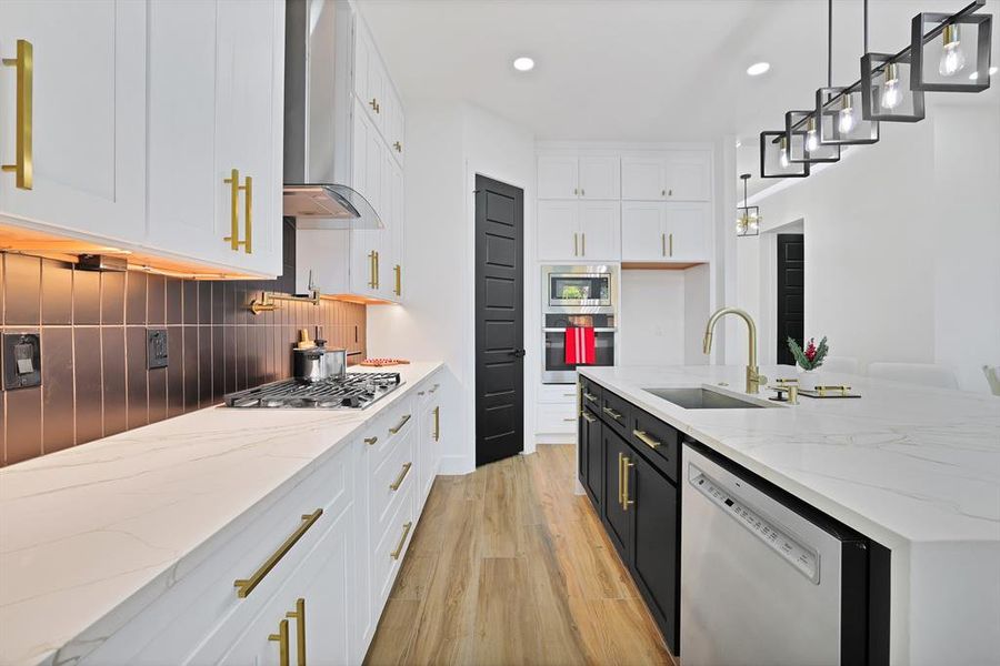 Kitchen with appliances with stainless steel finishes, wall chimney exhaust hood, sink, white cabinetry, and hanging light fixtures