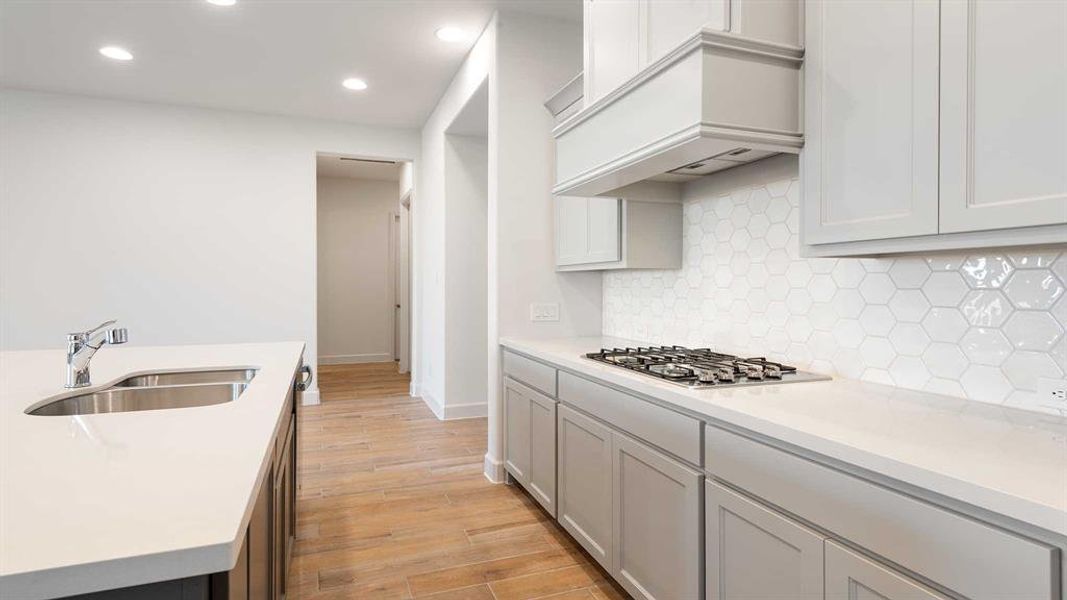 Kitchen featuring stainless steel gas cooktop, tasteful backsplash, sink, premium range hood, and light wood-type flooring