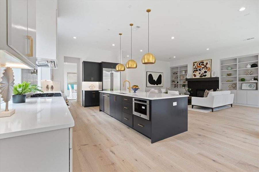 Kitchen featuring built in features, pendant lighting, light hardwood / wood-style flooring, a center island with sink, and sink