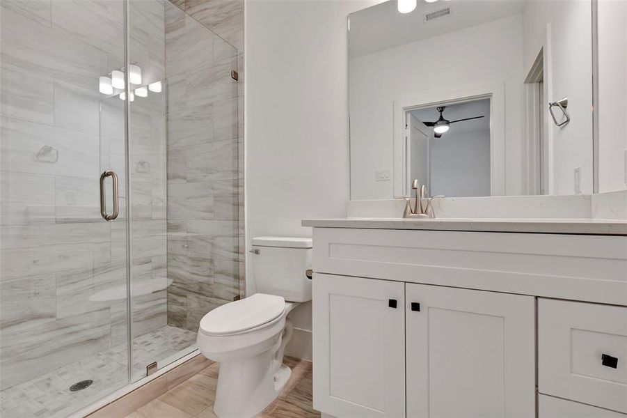 The first-floor en suite bathroom includes a stand-in shower enclosed with glass and offers additional storage with cabinets below the single sink with vanity space.