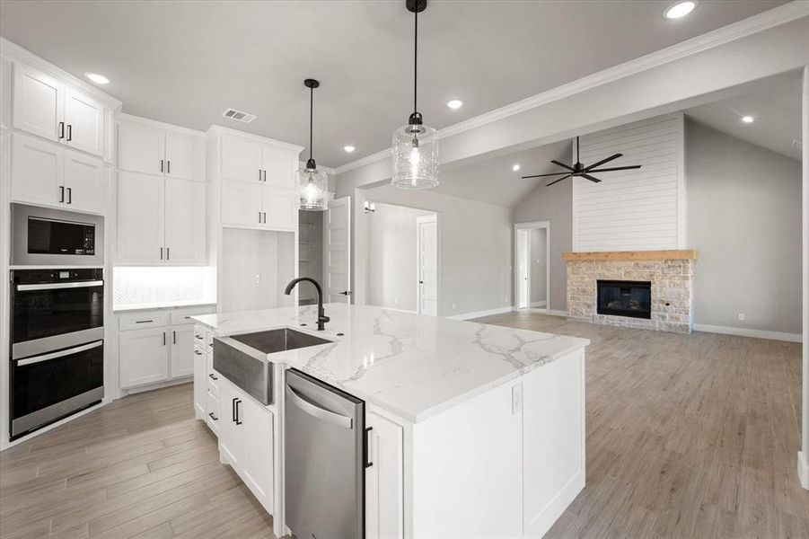 Kitchen featuring sink, a fireplace, white cabinetry, lofted ceiling, and a kitchen island with sink