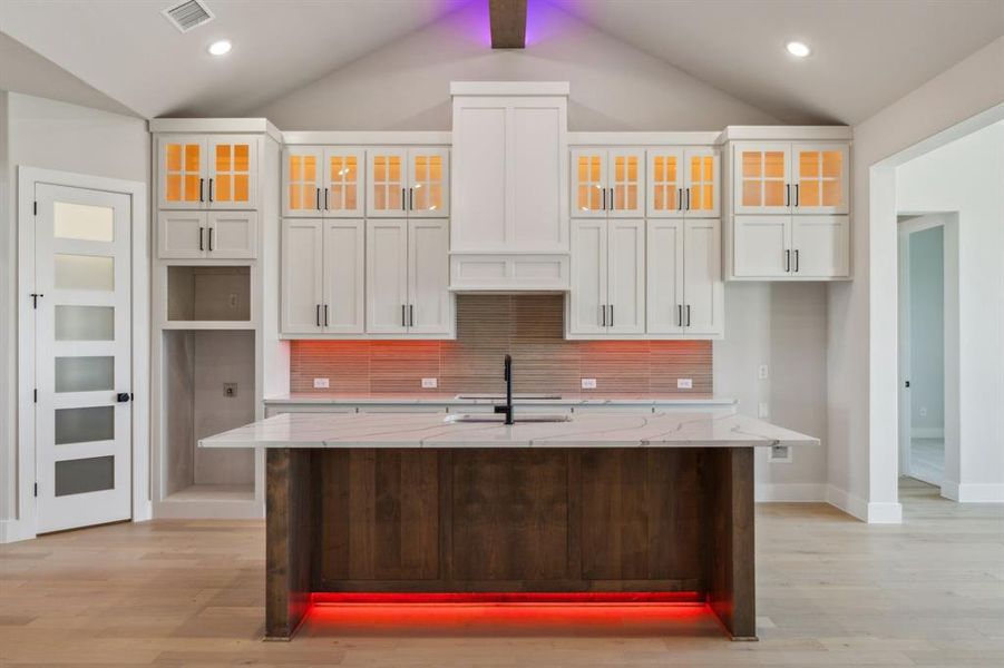 Kitchen with white cabinets, a center island with sink, light stone counters, and vaulted ceiling