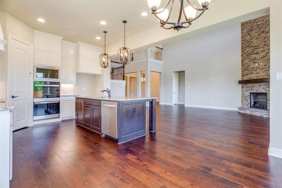 Kitchen featuring a stone fireplace, stainless steel appliances, dark wood-type flooring, and an inviting chandelier