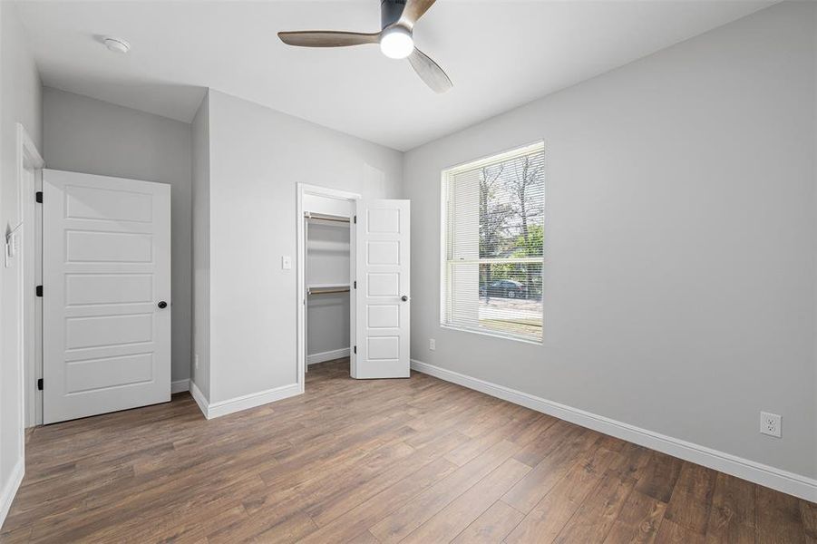 Unfurnished bedroom featuring dark wood-type flooring, a walk in closet, ceiling fan, and a closet