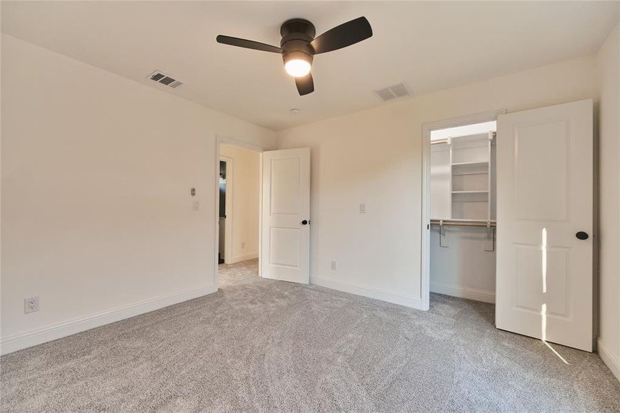 Unfurnished bedroom with light carpet, a closet, ceiling fan, and a walk in closet