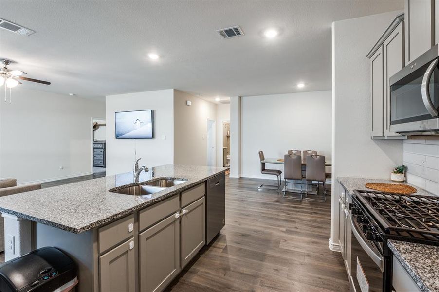 Kitchen with appliances with stainless steel finishes, sink, dark hardwood / wood-style flooring, gray cabinets, and a kitchen island with sink