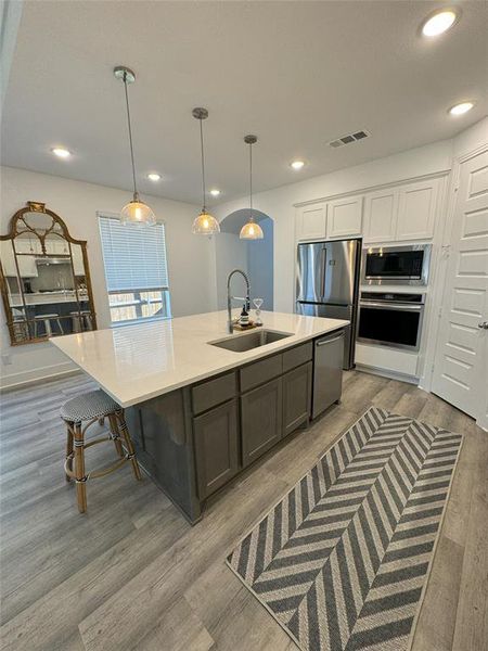 Kitchen with light hardwood / wood-style flooring, sink, pendant lighting, white cabinetry, and appliances with stainless steel finishes