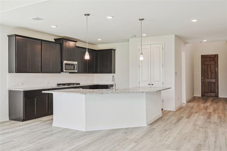 Kitchen with pendant lighting, light stone counters, a center island with sink, light hardwood / wood-style floors, and backsplash